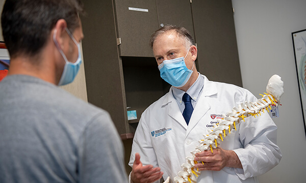 Physician describes a replica spine to a patient. Physician describes a replica spine to a patient.